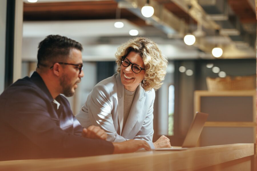 A man and a woman having a work discussion on a desk before a laptop.