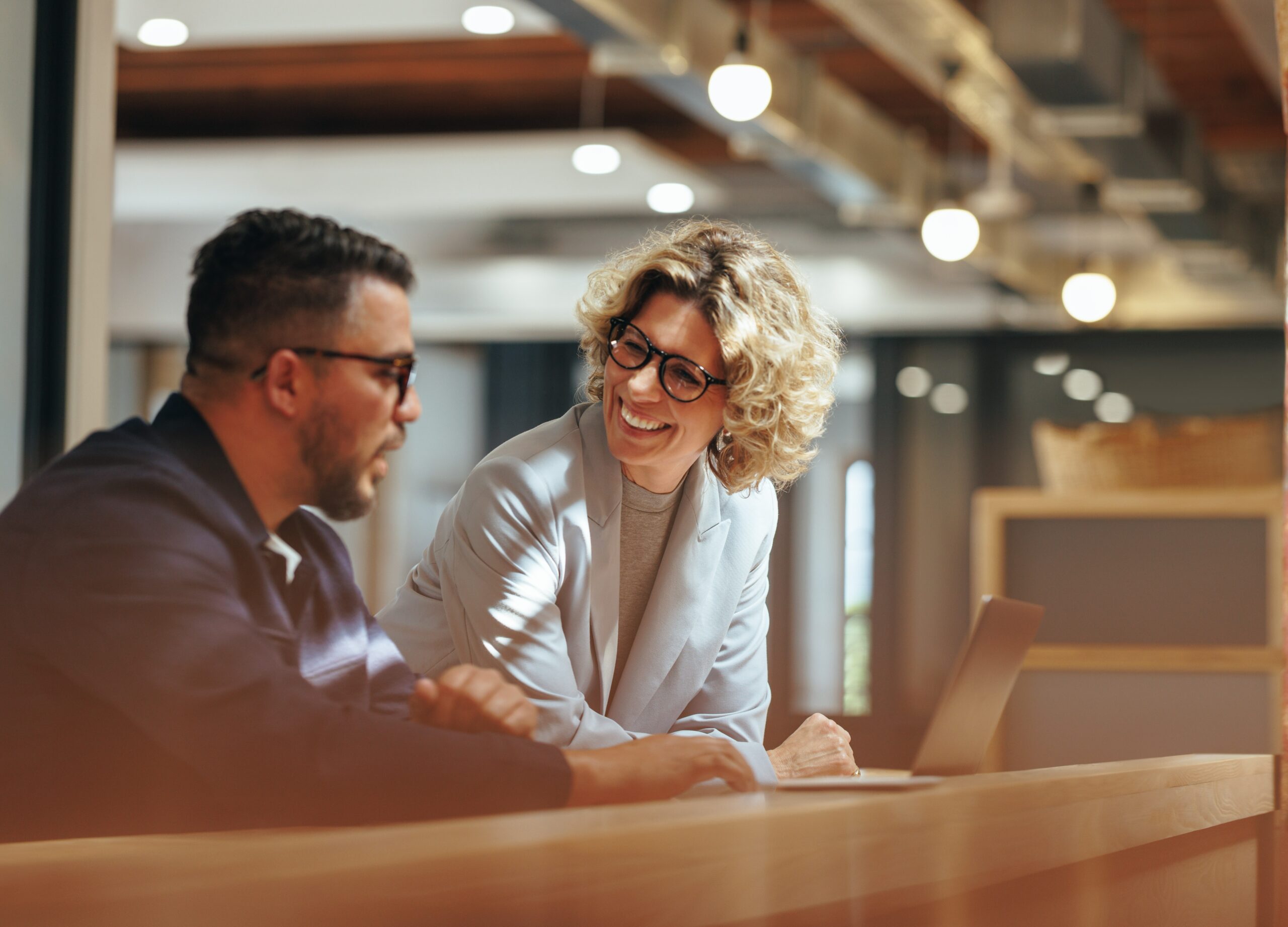 A man and a woman having a work discussion on a desk before a laptop.